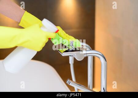 Mani femminili con gomma gialla guanti protettivi pulizia Miscelatore vasca con panno verde e spray detergente. Pulizia di Primavera Foto Stock