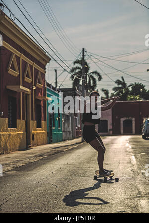 Giovane donna cavallo uno skateboard giù per una strada. Foto Stock