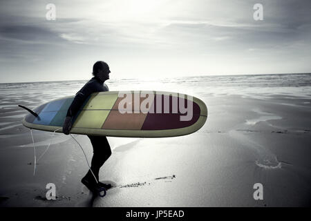 Vista laterale dell'uomo in mute a piedi dall'oceano, portando la tavola da surf. Foto Stock