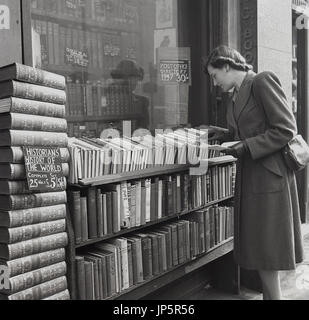 1948, storica, una giovane signora sfoglia le file di libri di seconda mano sovrapposti all'esterno di una libreria antiquaria in Charing Cross Rd, Londra, Inghilterra, Regno Unito. Una serie completa di libri di History of the World, disponibili a £5,00. A 1947 direttore postale per il 30/- Foto Stock