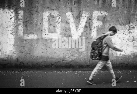 Scolaro camminando per la strada con la testa inchinata; amore sullo sfondo. Si torna a scuola. Foto Stock