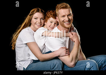 Ritratto di famiglia felice in bianco t-shirts abbraccia ogni altro isolato su nero Foto Stock