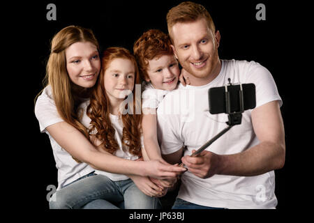 La famiglia felice tenendo selfie sullo smartphone isolato su nero Foto Stock