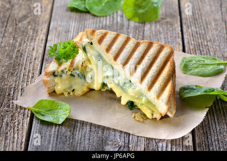 Premuto vegetariano panini doppia con giovani foglie di spinaci, cipolle e formaggio servita su carta a sandwich su un tavolo di legno Foto Stock