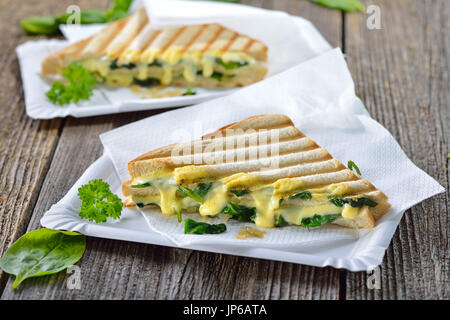 Premuto vegetariano panini doppia con giovani foglie di spinaci, cipolle e formaggio servita su piatti di carta su un tavolo di legno Foto Stock