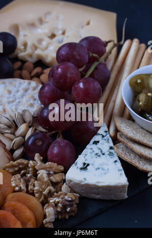 Formaggi assortiti, uva, crackers, dadi e oliva su sfondo nero Foto Stock