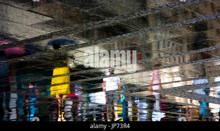 Sfocata riflessione silhouettes ombra di singole persone che camminano in una piovosa e soleggiata città di strada marciapiede pedonale in estate Foto Stock