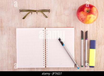 Vista superiore del notebook aperto con pagine vuote e matite, gli occhiali da lettura e apple sul tavolo di legno Foto Stock