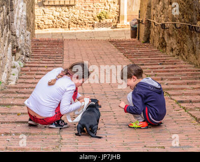 COLLE VAL D'elsa, Italia - 25 Aprile 2017 - Due bambini a giocare con un cucciolo di cane in un vicolo di Colle Val d'Elsa. Foto Stock