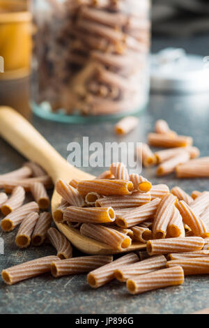 Essiccato rigatoni pasta sul cucchiaio di legno. Dark pasta di semola. Paste alimentari non cotte. Foto Stock