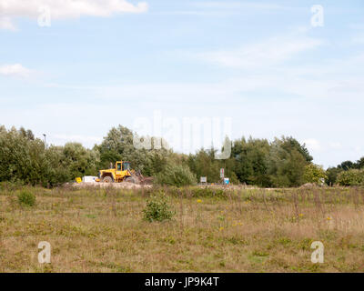 Giallo parcheggiato il trattore fermo nella distanza di campo al di fuori della cava di pietra arenaria; Essex, Regno Unito Foto Stock