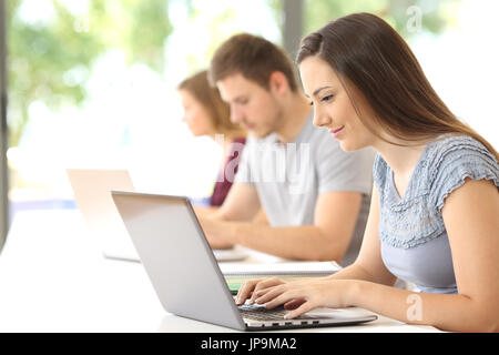 Vista laterale di un serio studente ricerca on line con un laptop a una classe Foto Stock