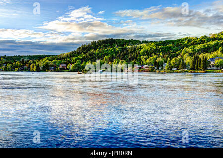 Chicoutimi nel fiume Saguenay, Quebec, Canada con il Riverfront case e foresta durante il tramonto Foto Stock