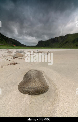 Roccia sulla spiaggia sabbiosa telai le nuvole scure sulle cime Unstad Vestvagøy Isole Lofoten in Norvegia Europa Foto Stock