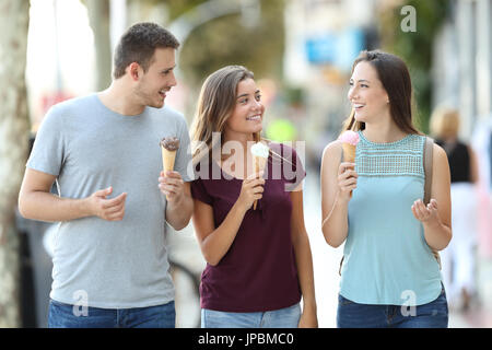 Vista frontale di tre amici felice di parlare e mangiare gelati a piedi in strada Foto Stock