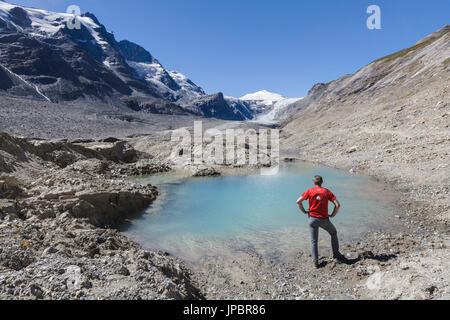 Europa Austria, Carinzia, Glockner Gruppo, Alti Tauri. Un uomo lookin per Johannisberg mountain nei pressi di un laghetto di acqua sul ghiacciaio Pasterze a Grossglockner Foto Stock