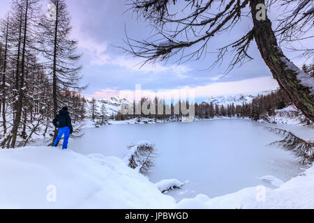 Escursionista ammira il Lago Azzurro completamente congelato all'alba Valle Spluga Provincia di Sondrio Valtellina Lombardia Italia Europa Foto Stock