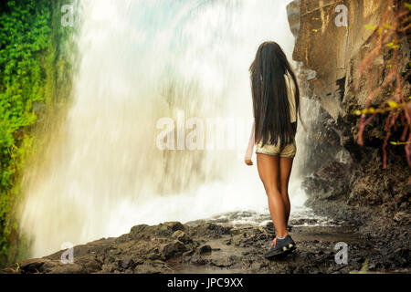 Ragazza ammira molto grande e bella cascata in Indonesia. Ragazza viaggia per il mondo.incredibilmente bella cascata nella giungla di Indonesia. Una ragazza di stand Foto Stock