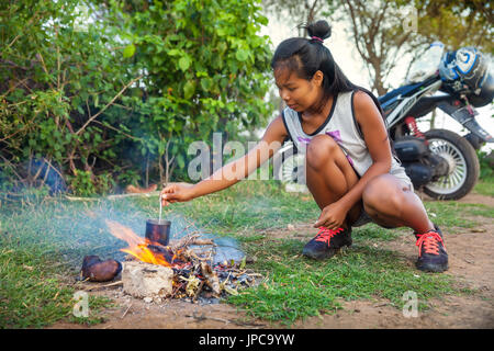 Giovane bella ragazza di viaggio zaino in spalla per la cottura sul fuoco alimenti per la colazione con caffè fresco su sfondo natura tropicale e campeggio Foto Stock