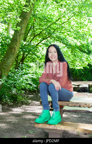 Donna seduta su un tavolo da pic-nic nel bosco Foto Stock