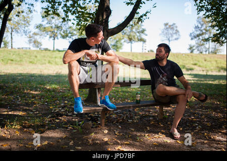 Due amici a parlare nel parco e sedersi sul banco di lavoro Foto Stock