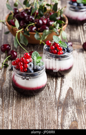 Estate dessert di yogurt con ciliege acide, ribes rosso e mirtillo gelatina e decorate con frutti di bosco freschi Foto Stock