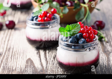 Estate dessert di yogurt con ciliege acide, ribes rosso e mirtillo gelatina e decorate con frutti di bosco freschi Foto Stock