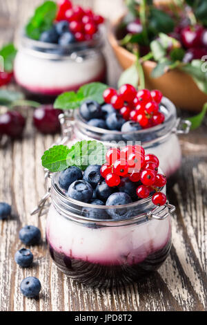 Estate dessert di yogurt con ciliege acide, ribes rosso e mirtillo gelatina e decorate con frutti di bosco freschi Foto Stock