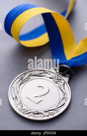 Close-up studio shot del secondo posto medaglia d argento con strisce blu e nastro giallo su sfondo grigio Foto Stock