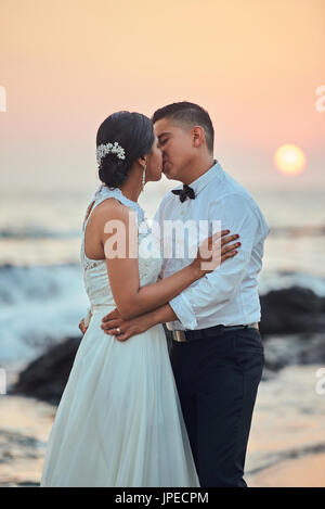 Coppie in viaggio di nozze baciare sulla spiaggia al tramonto del tempo. Sposa e lo sposo kiss Foto Stock