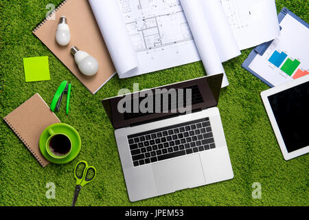 Il luogo di lavoro con casco, blueprint, laptop e blocco note su sfondo di erba. Vista da sopra con lo spazio di copia Foto Stock