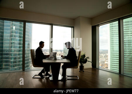 Due imprenditori negoziando seduti ad un tavolo per conferenza in modernamente Foto Stock