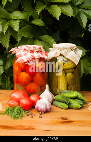 Conserve e verdure fresche. Conserve di pomodori e cetrioli sottaceto in vasetti di vetro sul tavolo in legno all'esterno. In Casa Conserve di verdura. Foto Stock