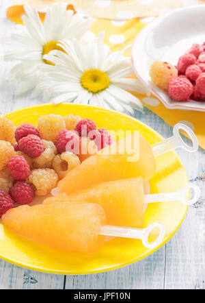 Gelato di frutta Lampone giallo con i frutti di bosco Lamponi su una piastra sullo sfondo di grandi margherite. Close-up. Il telaio verticale. Foto Stock