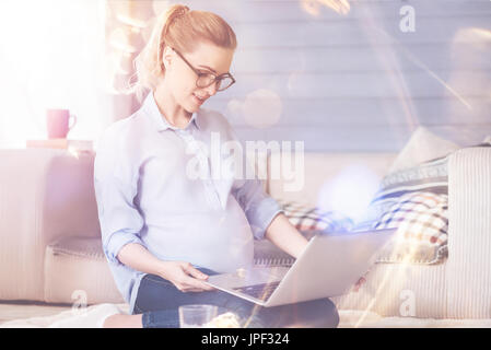Piacevole donna incinta utilizzando laptop Foto Stock