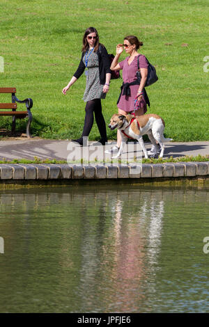 Abington Park, Northampton, meteo, 1 agosto 2017. Il sole di questa mattina con la luce delle nuvole e ora di nuovo la previsione per il giorno. 2 amiche a piedi un cane intorno al lago in barca sotto il sole. Credito: Keith J Smith./Alamy Live News Foto Stock