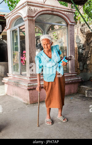 Un anziano, bianco-pelose vecchia donna filippina vende candele votive al di fuori la sua chiesa in Bogo Città, isola di Cebu, Filippine. Foto Stock