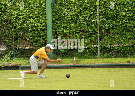 Uomo cinese facendo rotolare una palla in gioco di bocce su prato su un campo di bocce in Hong Kong Foto Stock