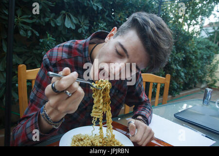 Giovani intraprendenti boy mangiare ramen a pranzo. Egli è in appoggio un mentre dal lavoro per raccogliere energie. Foto Stock