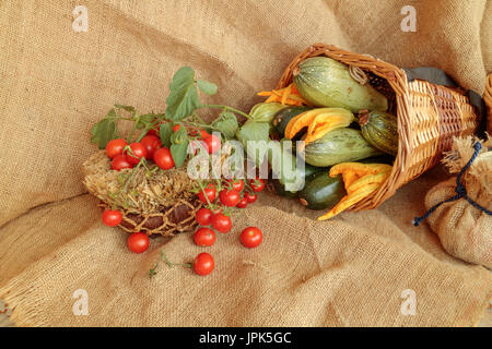 Zucchine e pomodori ciliegia harvest scena sulla iuta. Ancora vegetale composizione di vita Foto Stock