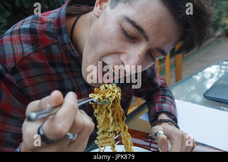 Giovani intraprendenti boy mangiare ramen a pranzo. Egli è in appoggio un mentre dal lavoro per raccogliere energie. Foto Stock