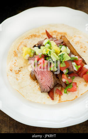 Le fajitas di manzo con salsa di pomodoro Pico de Gallo e guacamole servito su tortilla su piastra bianca. Tradizionale cibo messicano. Messa a fuoco selettiva, primo piano Foto Stock