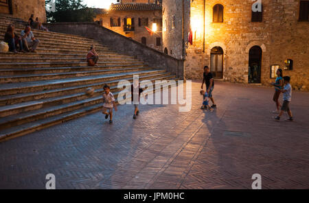 Poco italiano i ragazzi che giocano a calcio la sera su una strada della splendida città medievale di San Gimignano, Italia Foto Stock