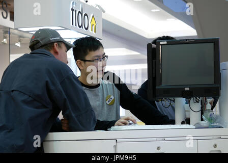 Persone che chiedono fido addetto alle vendite su cellulare all'interno del piano Burnaby shopping mall Foto Stock