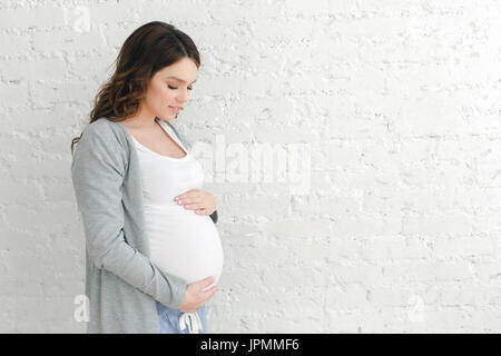 Donna incinta toccando ventre su sfondo bianco Foto Stock