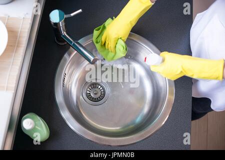 Donna con le mani in mano in giallo i guanti di gomma il lavaggio del lavello in cucina - vista superiore Foto Stock