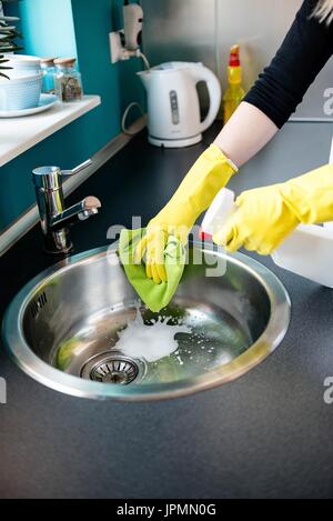 Donna con le mani in mano in giallo i guanti di gomma il lavaggio del lavello in cucina Foto Stock