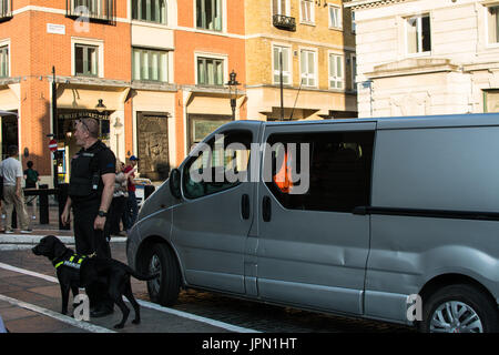 Un agente di polizia con cane da cecchino si trova accanto a un furgone d'argento durante una pattuglia di routine nel centro di Londra, Inghilterra, Covent Garden, Londra Foto Stock