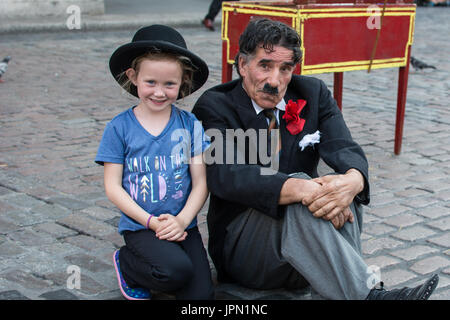 Covent Garden London ragazza con clown con cappello di bocciaio Charlie Chaplin Lookalike persona stile cappello ragazza bambino uomo baffi fiore vestito posh Foto Stock