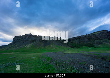 Islanda - luminoso Nuvoloso Tramonto sulle montagne dietro il verde paesaggio Foto Stock